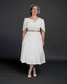 Woman wearing a white dress with a fur shrug and hat against a dark background. This dress is the Upton Dress & Skirt sewing pattern from Cashmerette.
