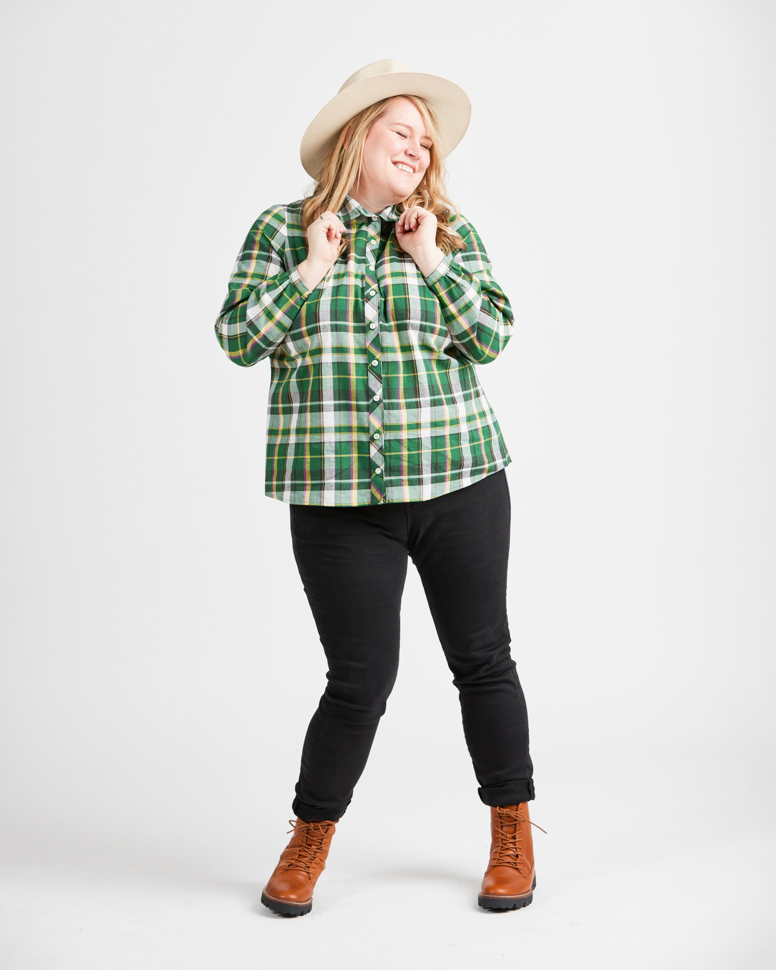 Woman wearing a green plaid shirt, black pants, and brown boots on a white background. This top is the Vernon Shirt sewing pattern from Cashmerette.