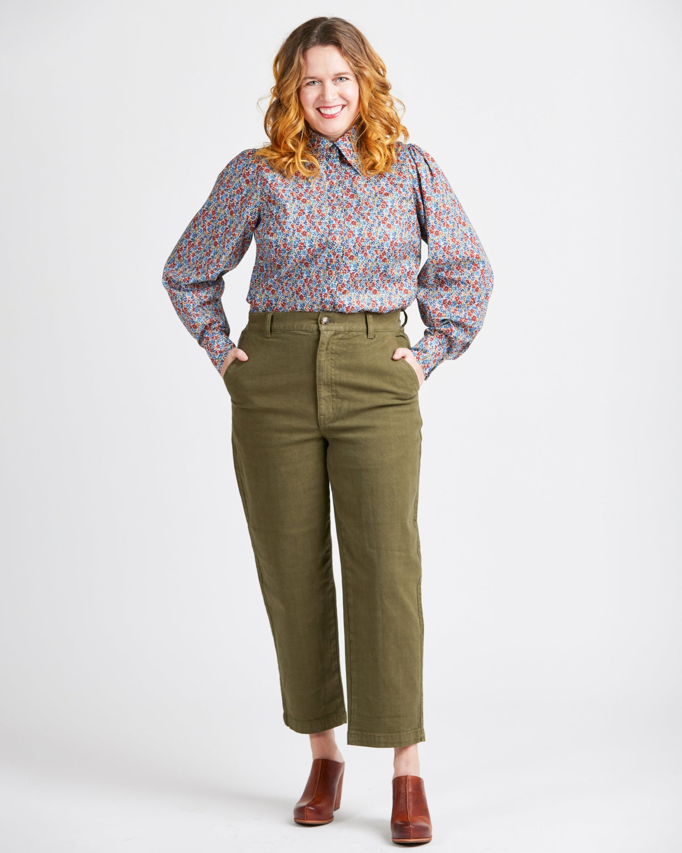 Woman wearing a floral blouse and green pants on a white background. This top is the Vernon Shirt sewing pattern from Cashmerette.