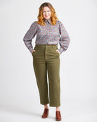 Woman wearing a floral blouse and green pants on a white background. This top is the Vernon Shirt sewing pattern from Cashmerette.